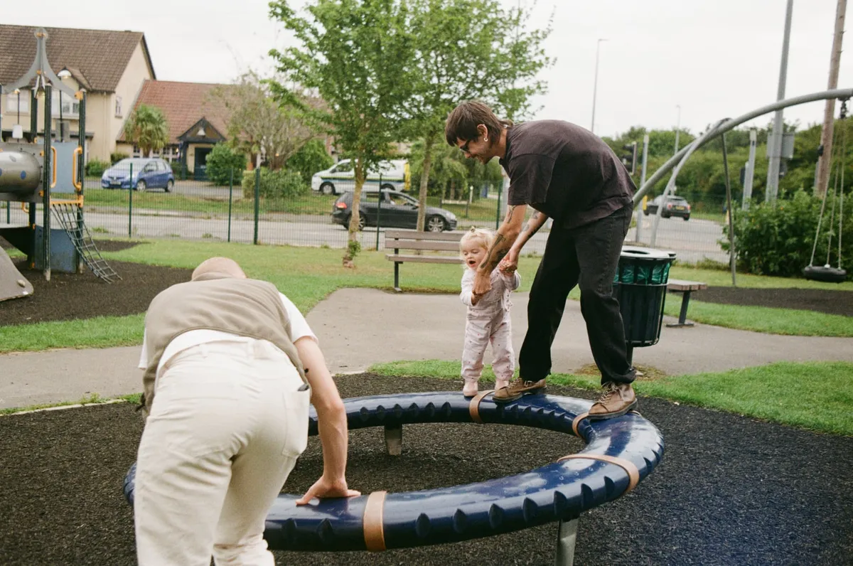 A family pushing a child on a playground roundabout