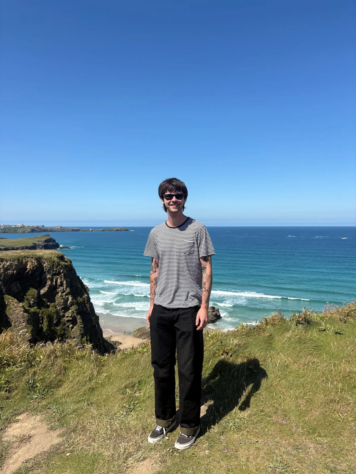 Josh standing on a clifftop above the sea on a sunny day