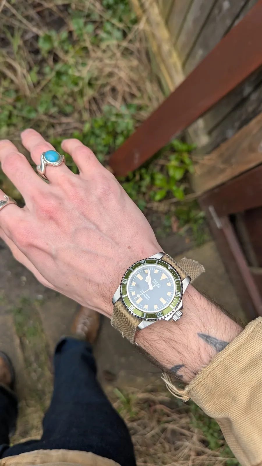 A hand with a turquoise ring and a green-dial watch